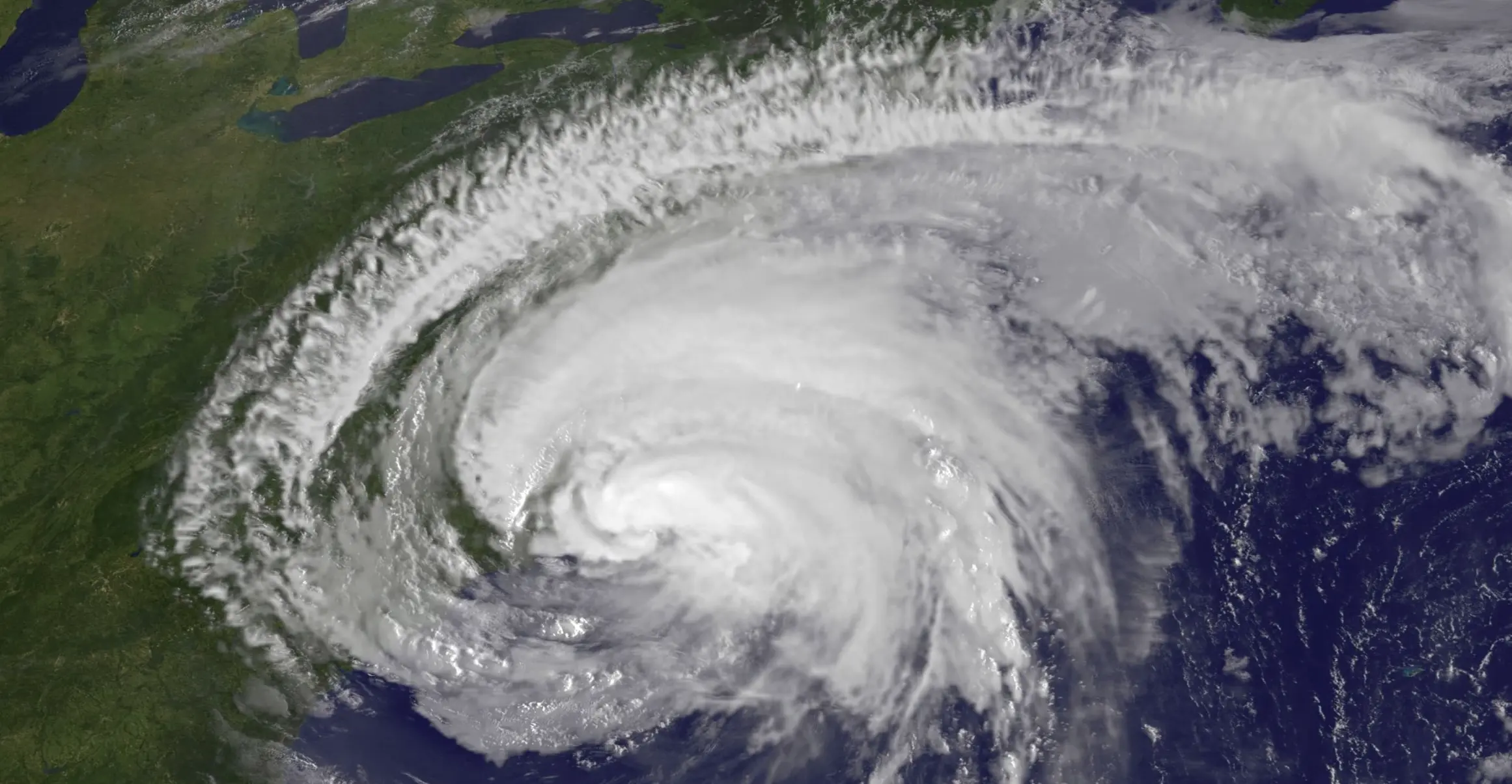 Satellite image of a large hurricane swirling over the Atlantic Ocean near the eastern coast of North America, with dense clouds and a visible eye.